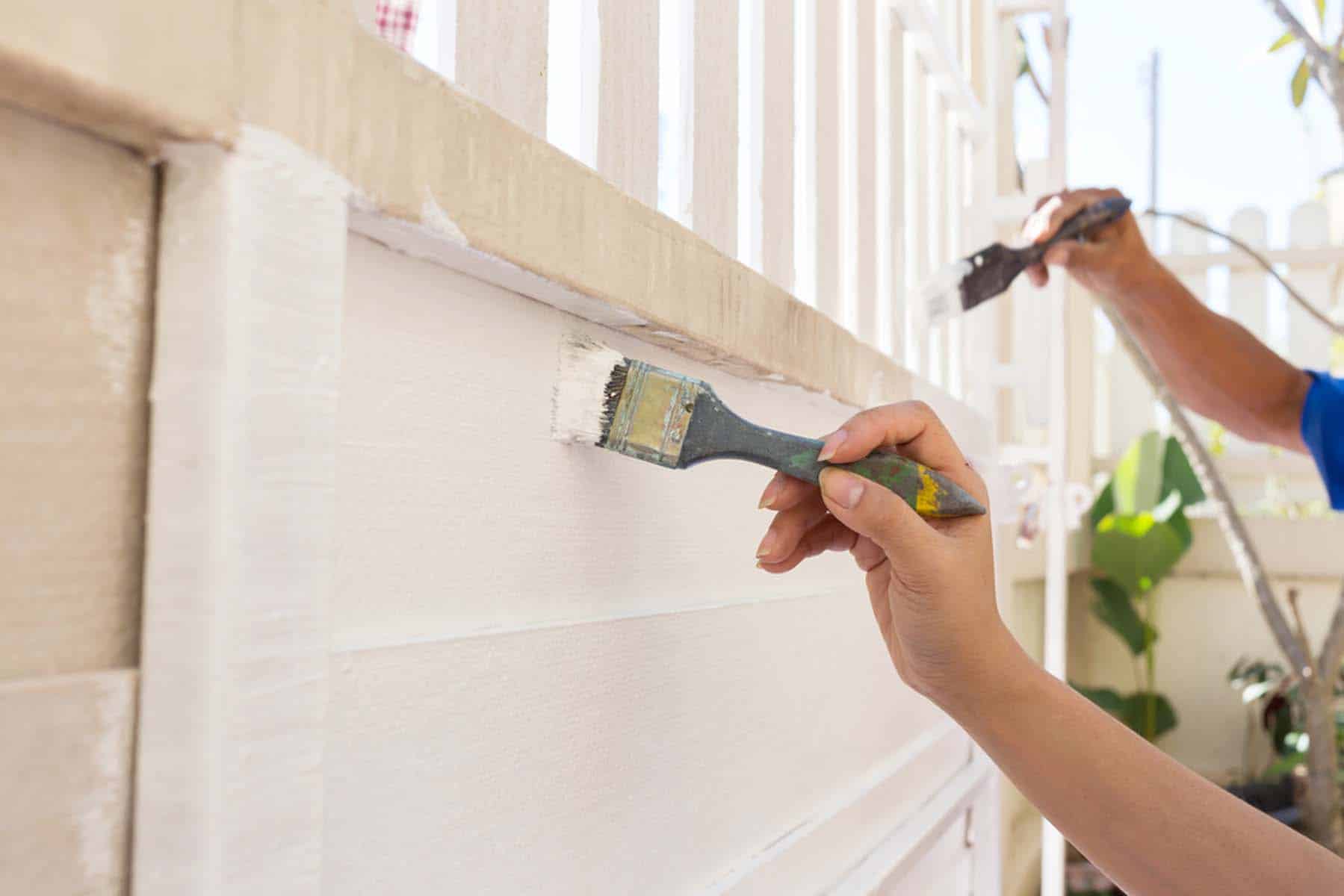 A brush cutting in fresh white paint along wood siding