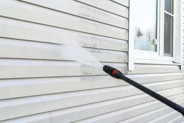 A pressure washer lifting dirt from the siding of a house