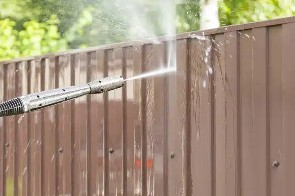 A pressure washer cleaning a wood fence panel