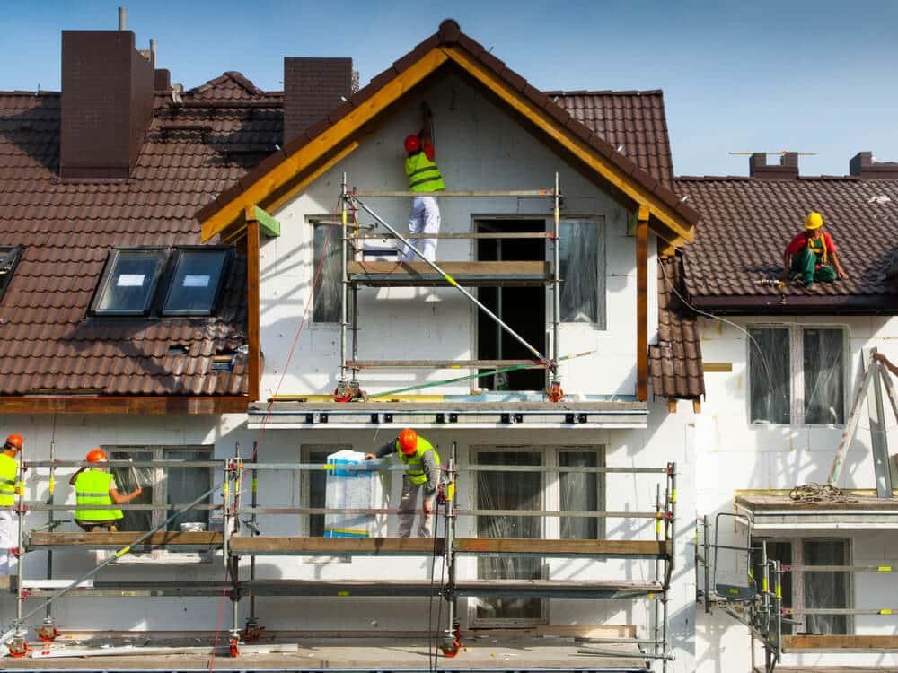 A crew on a scaffold working across the upper floor of a house exterior