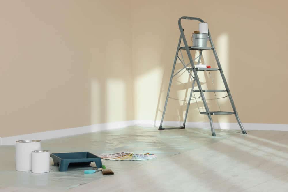 An empty room cleared for painting with a stepladder and a paint tray on the floor