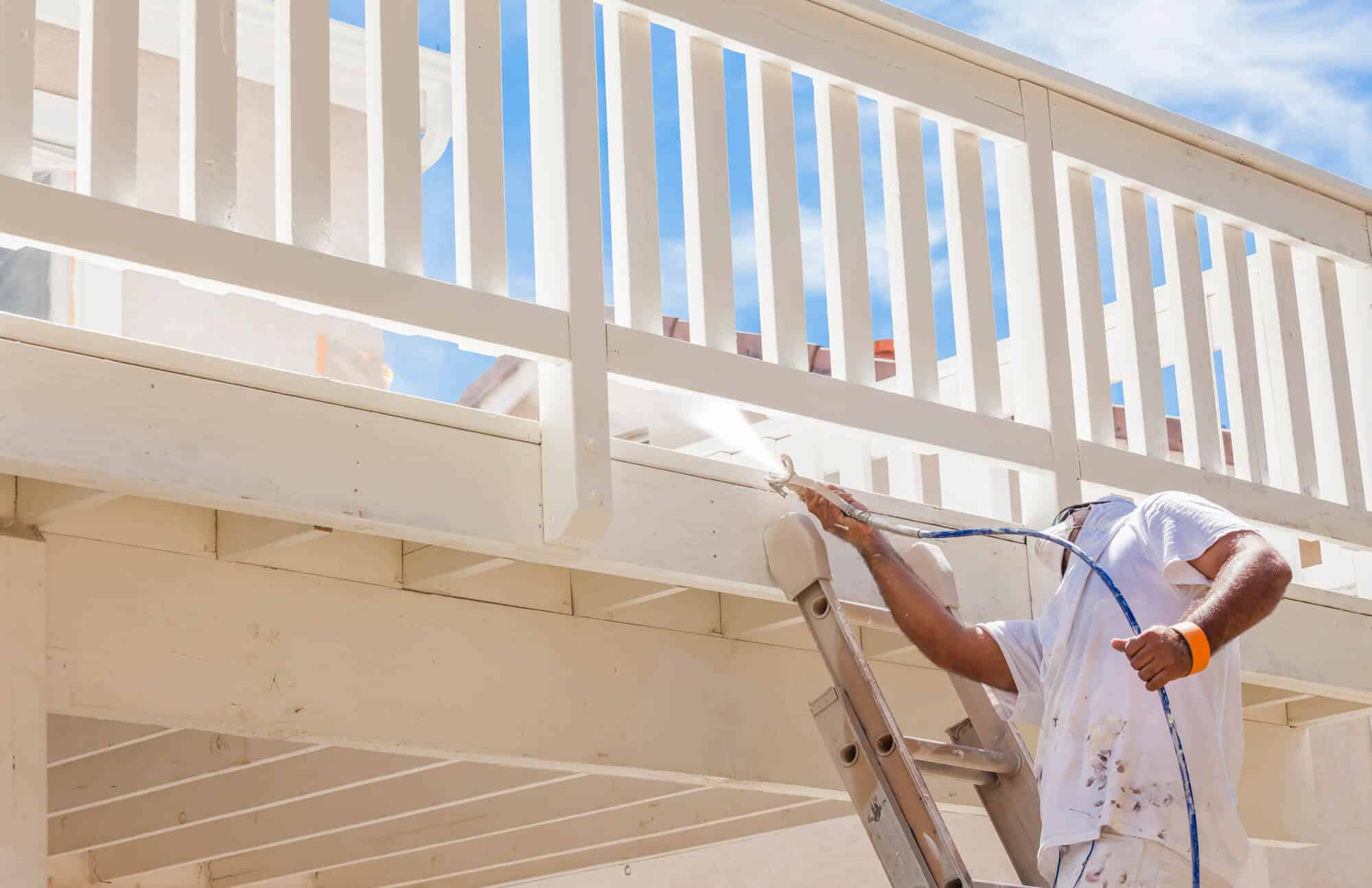 A painter coating a deck railing in white