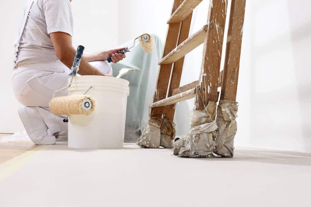 A painter kneeling to cut in along the bottom of a wall