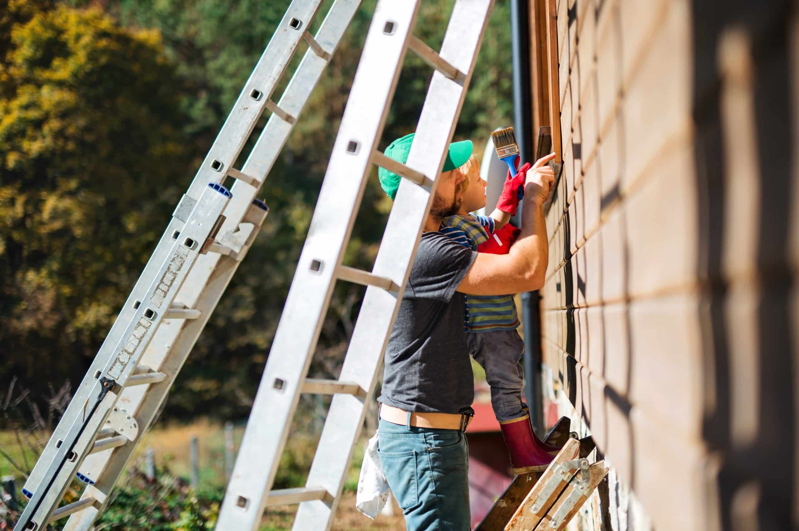 A painter on a ladder working along the brick and timber of a house exterior