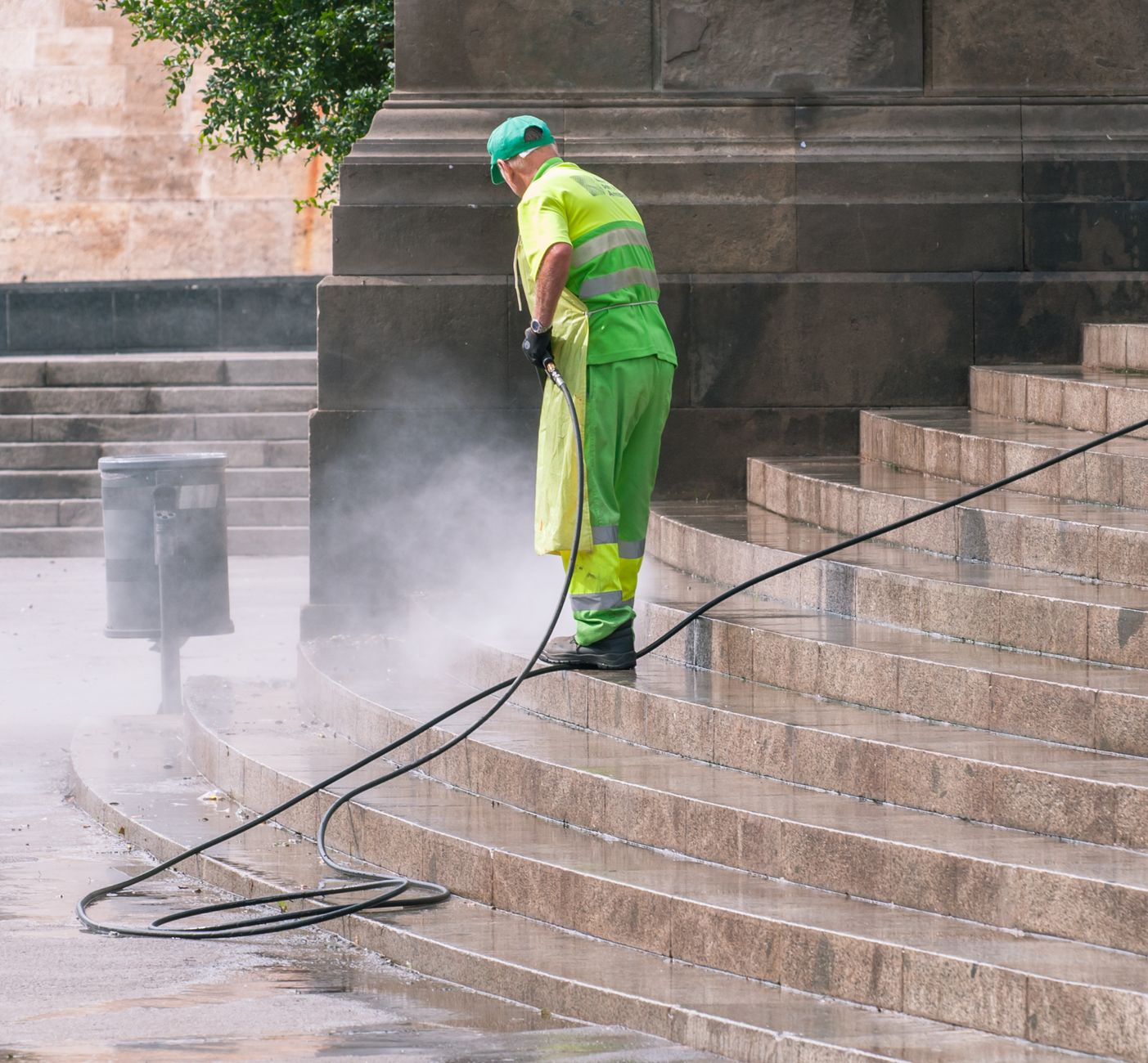 A worker pressure-washing stone steps outside a building