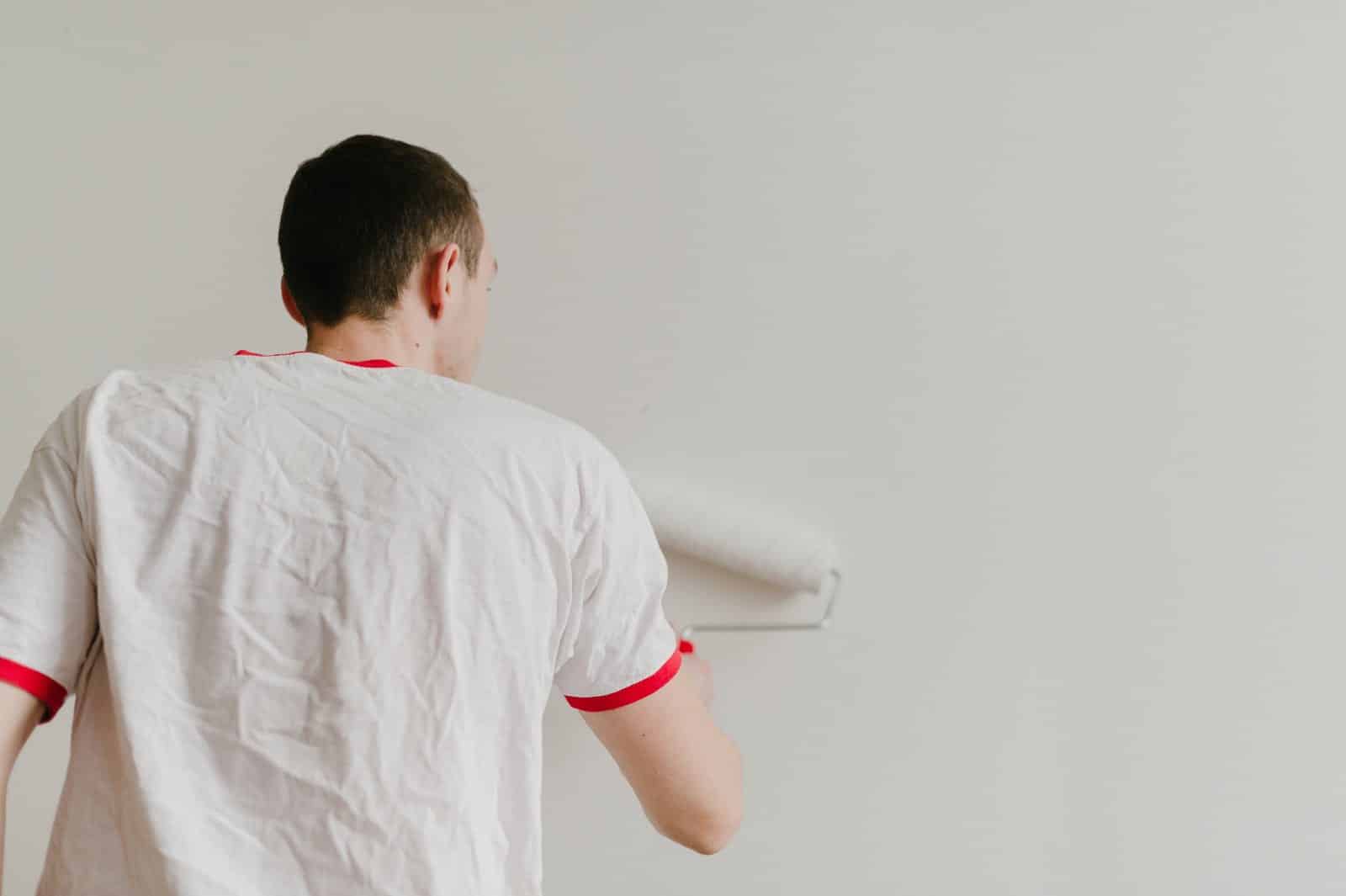 A painter seen from behind rolling paint onto a wall
