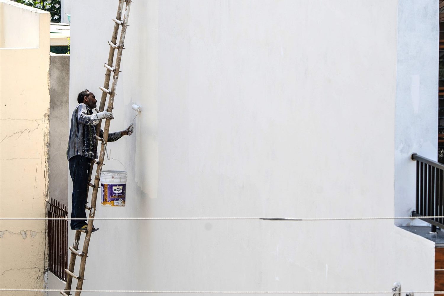 A painter on a ladder coating the outside wall of a building