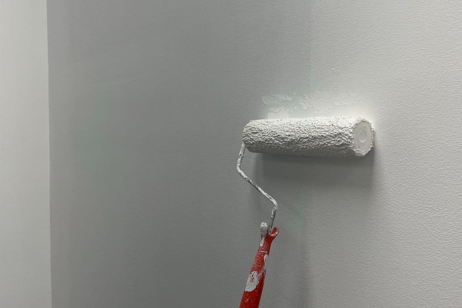A roller laying fresh white paint on an interior wall