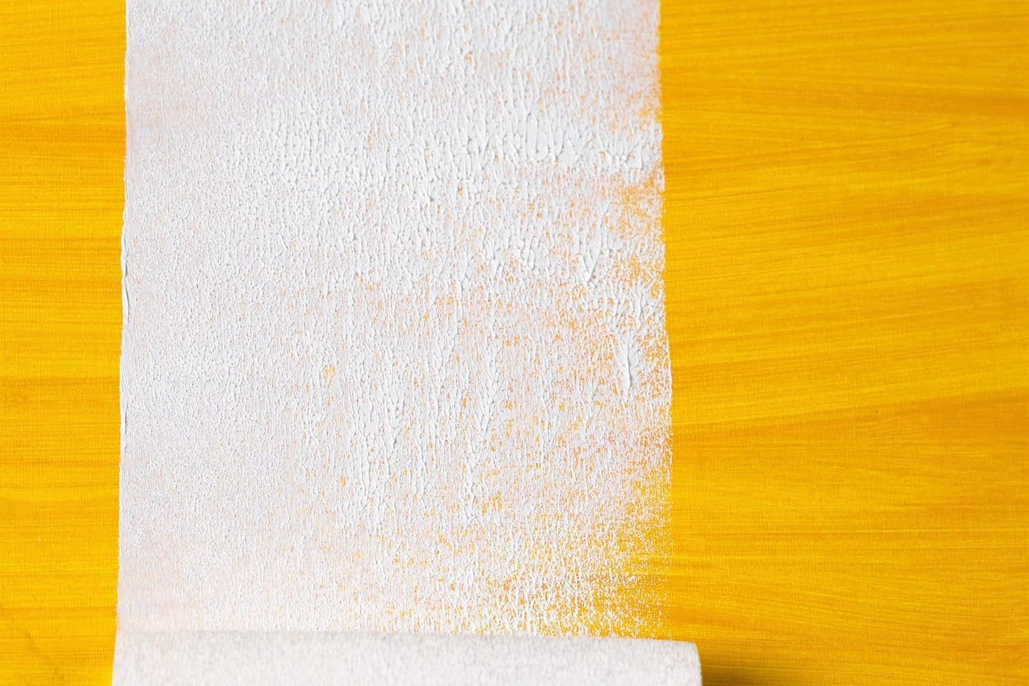 A roller cutting a pale stripe across a yellow wall