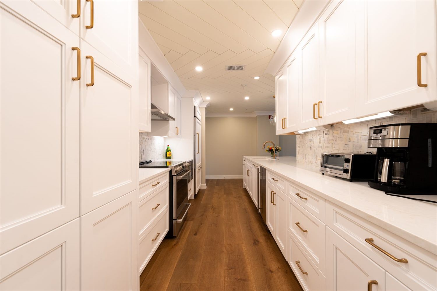 A narrow kitchen with white cabinets and a wooden floor