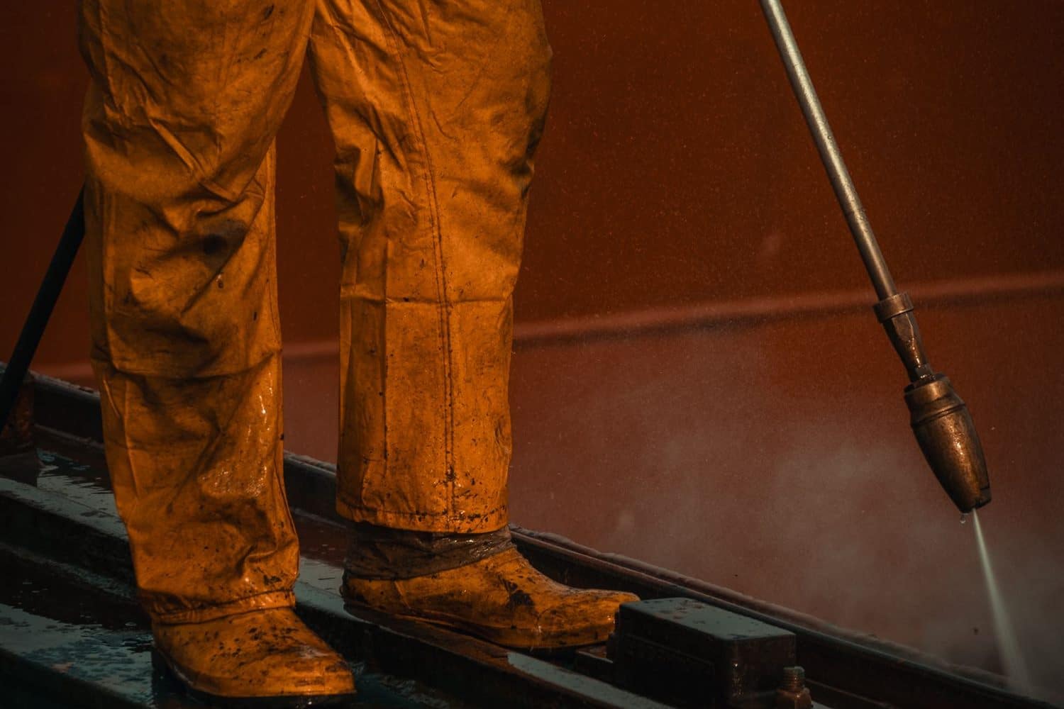 A worker in overalls washing a hard surface with a lance