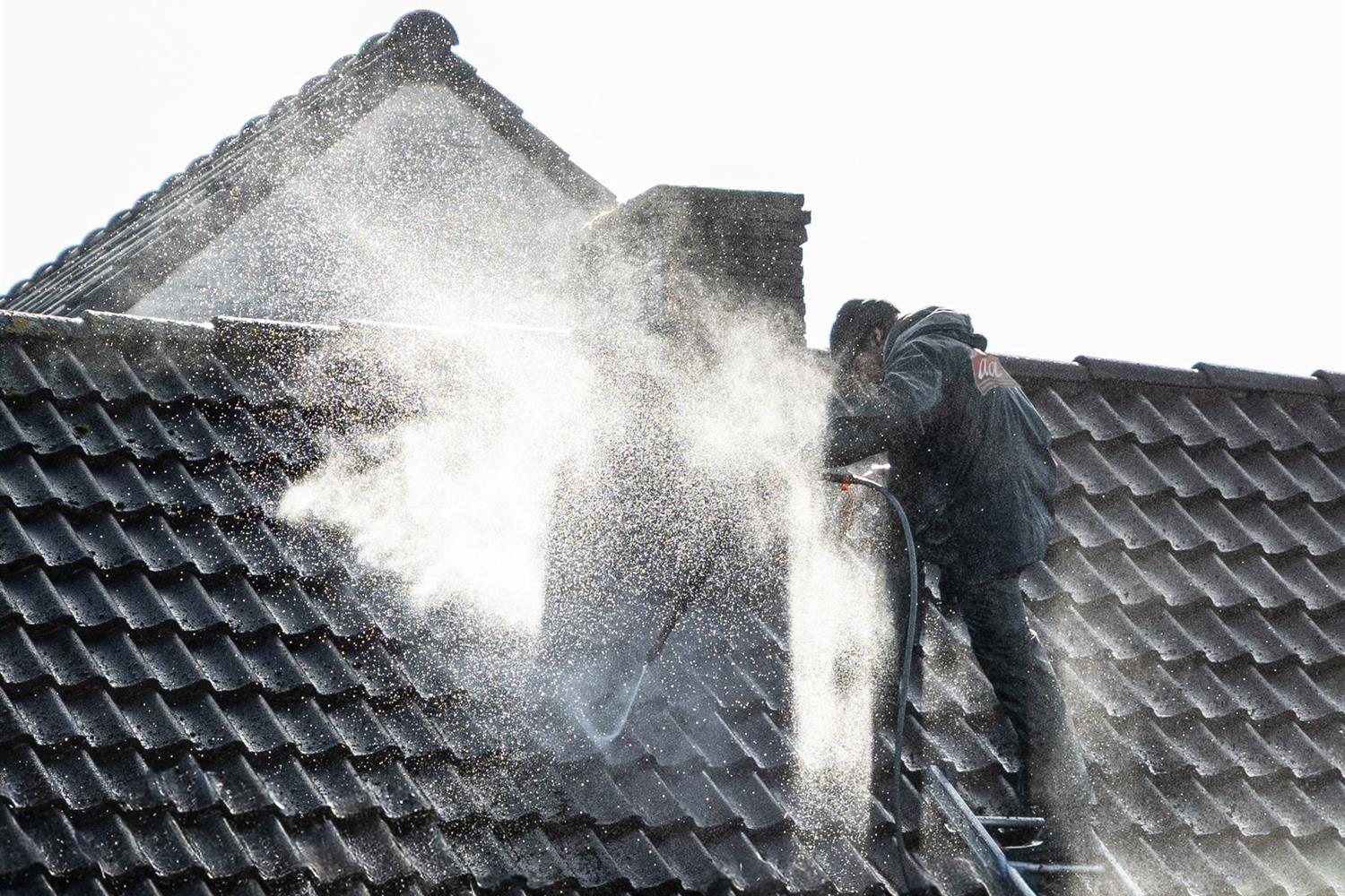 A worker washing grime off a tiled roof