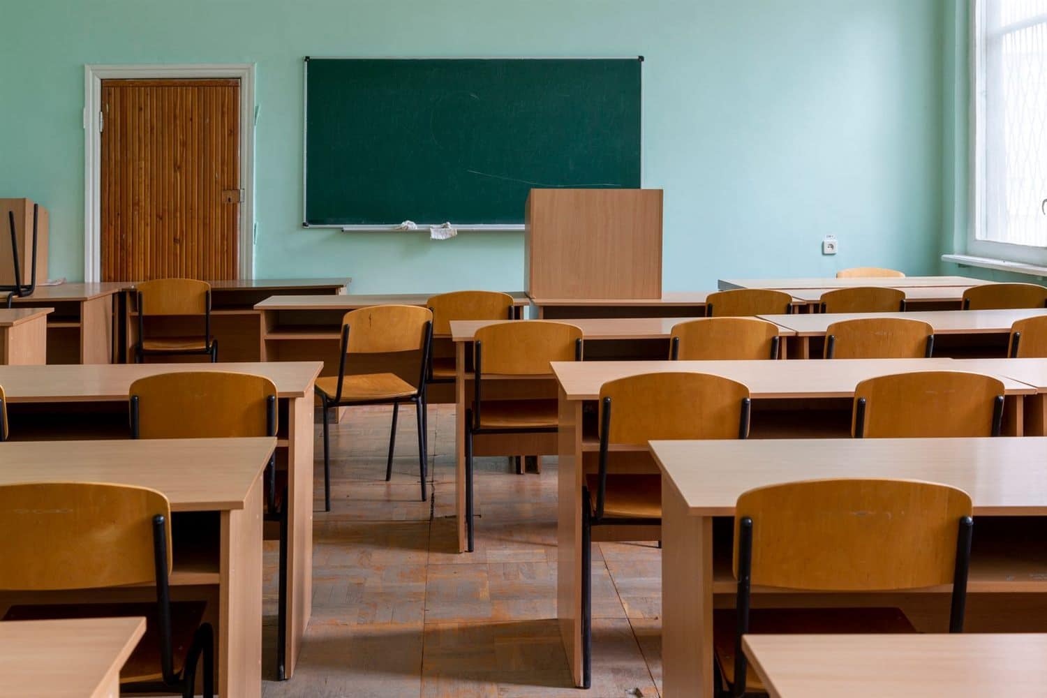 An empty classroom with wooden desks and a chalkboard