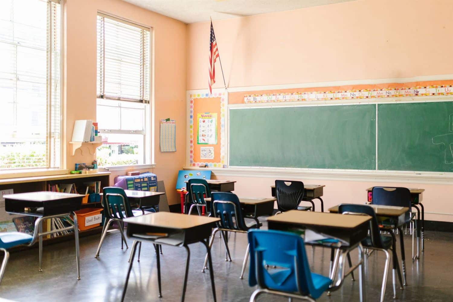 A sunlit classroom with desks and a green chalkboard