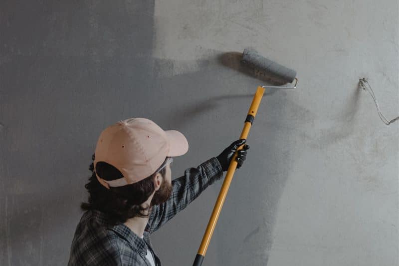 A painter laying a coat of gray paint with a pole roller