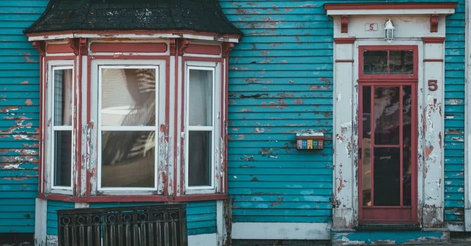 Older wood-sided home in New Orleans with peeling blue exterior paint around a bay window and door