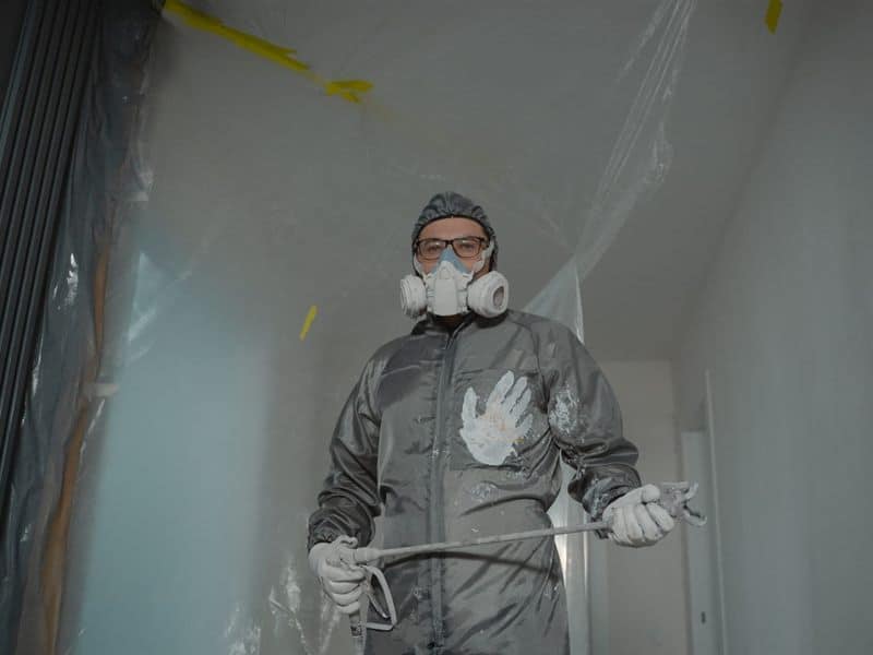 A painter in a protective suit and respirator working inside a contained area