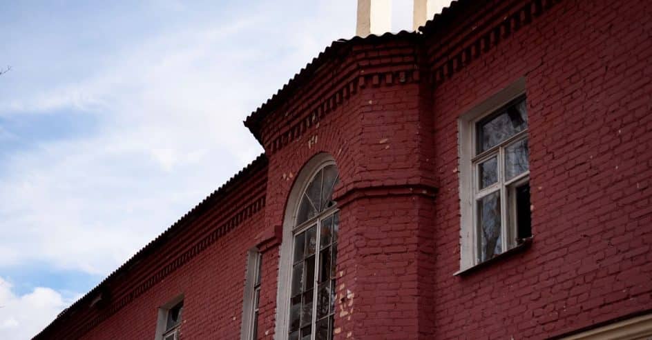 Painted red brick building exterior with arched window, showing masonry ready for repainting