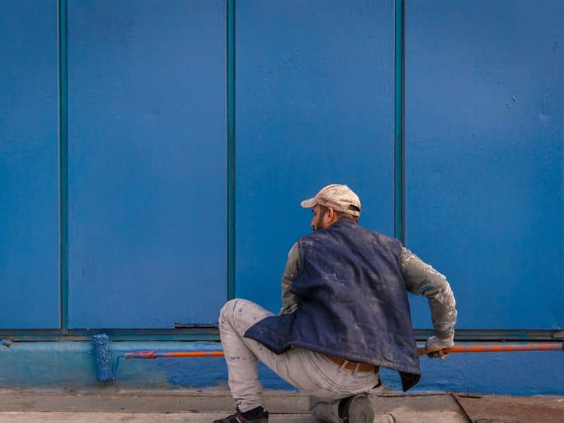 A painter coating the masonry wall of a commercial building