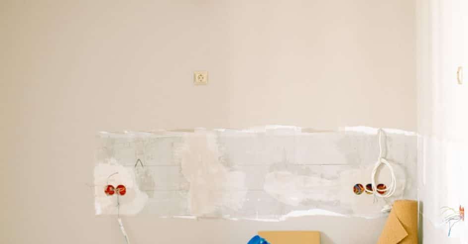 Interior wall stripped and patched before painting, with paint cans and tools on the floor